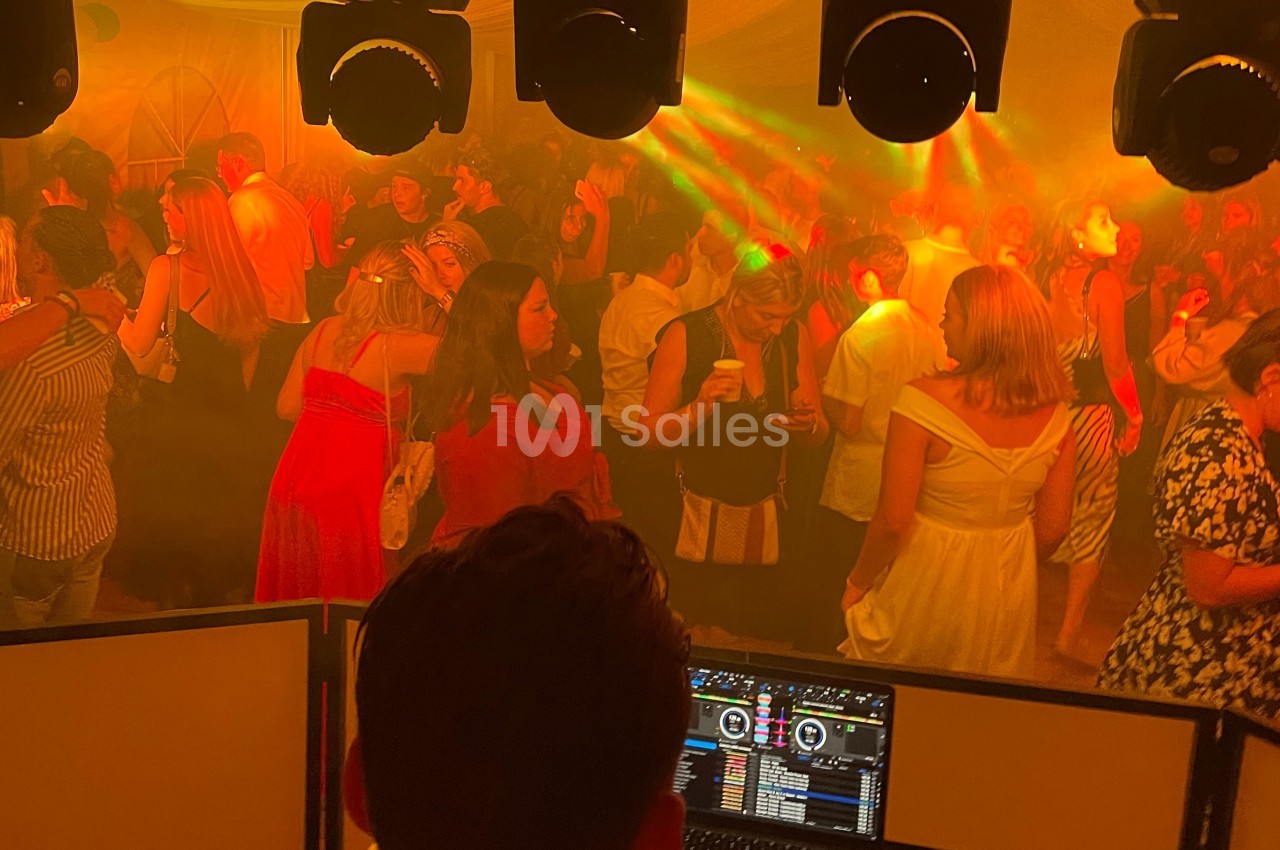 Vue depuis la cabine d’un DJ sur une foule dansante sous des lumières colorées dans une ambiance festive.