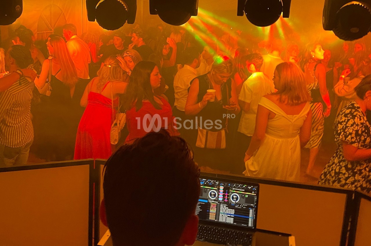 Personnes dansant et discutant dans une ambiance festive avec éclairages colorés, vue depuis la cabine du DJ.