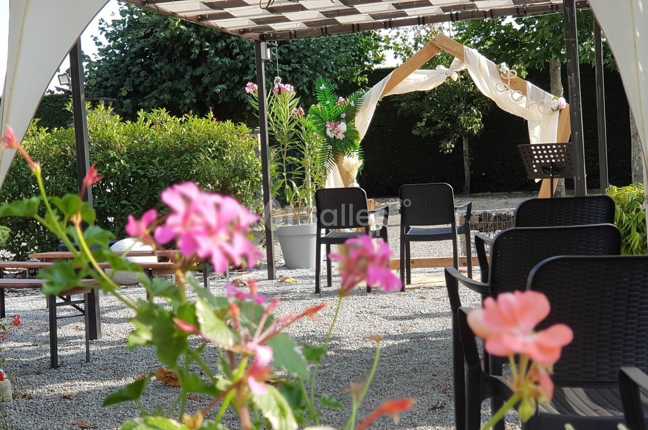 Chaises disposées sous une pergola en extérieur, avec des fleurs au premier plan et une arche décorée en arrière-plan.