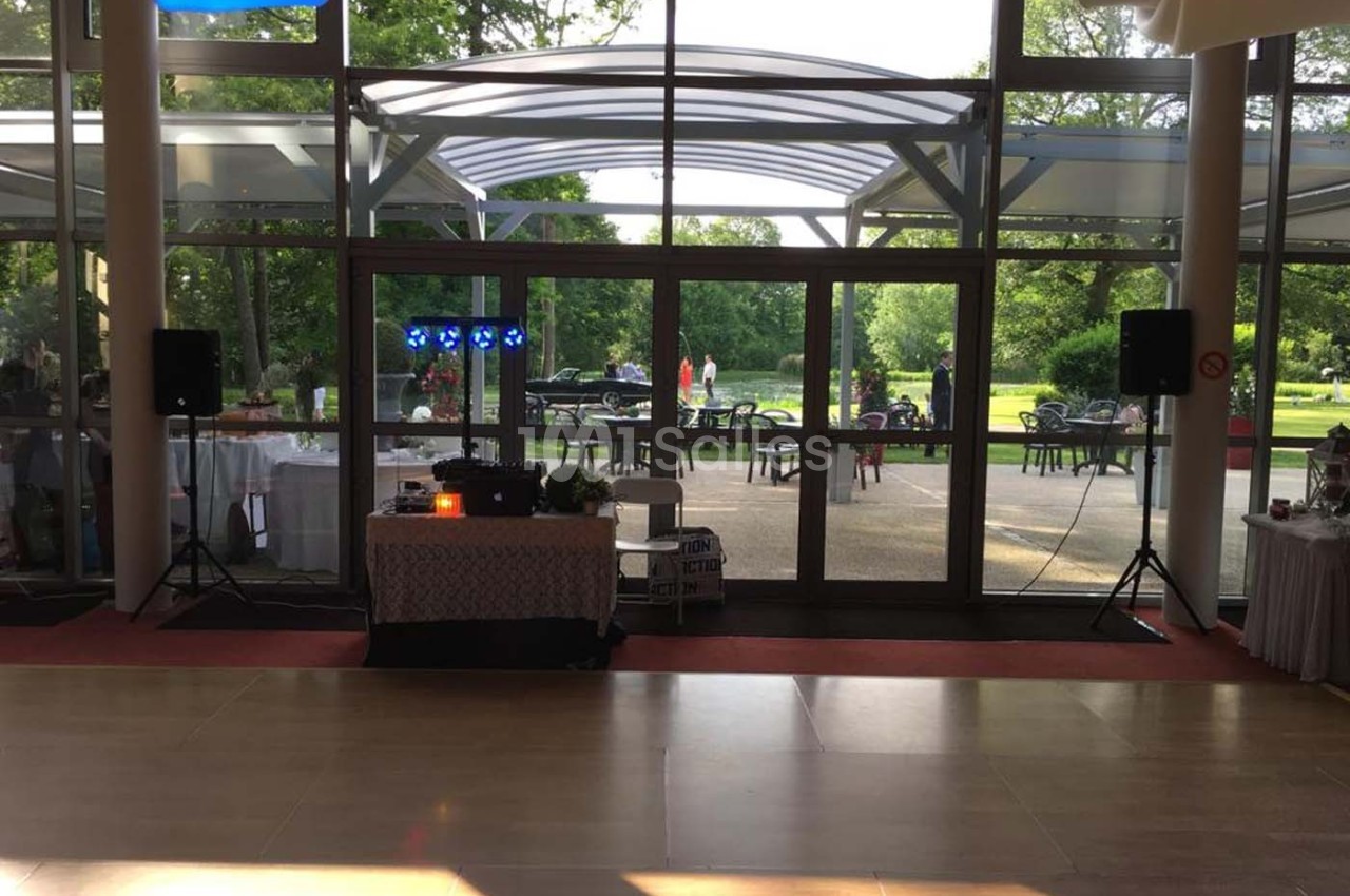 Salle lumineuse avec baie vitrée donnant sur un jardin, équipée d'une table de mixage et de haut-parleurs.