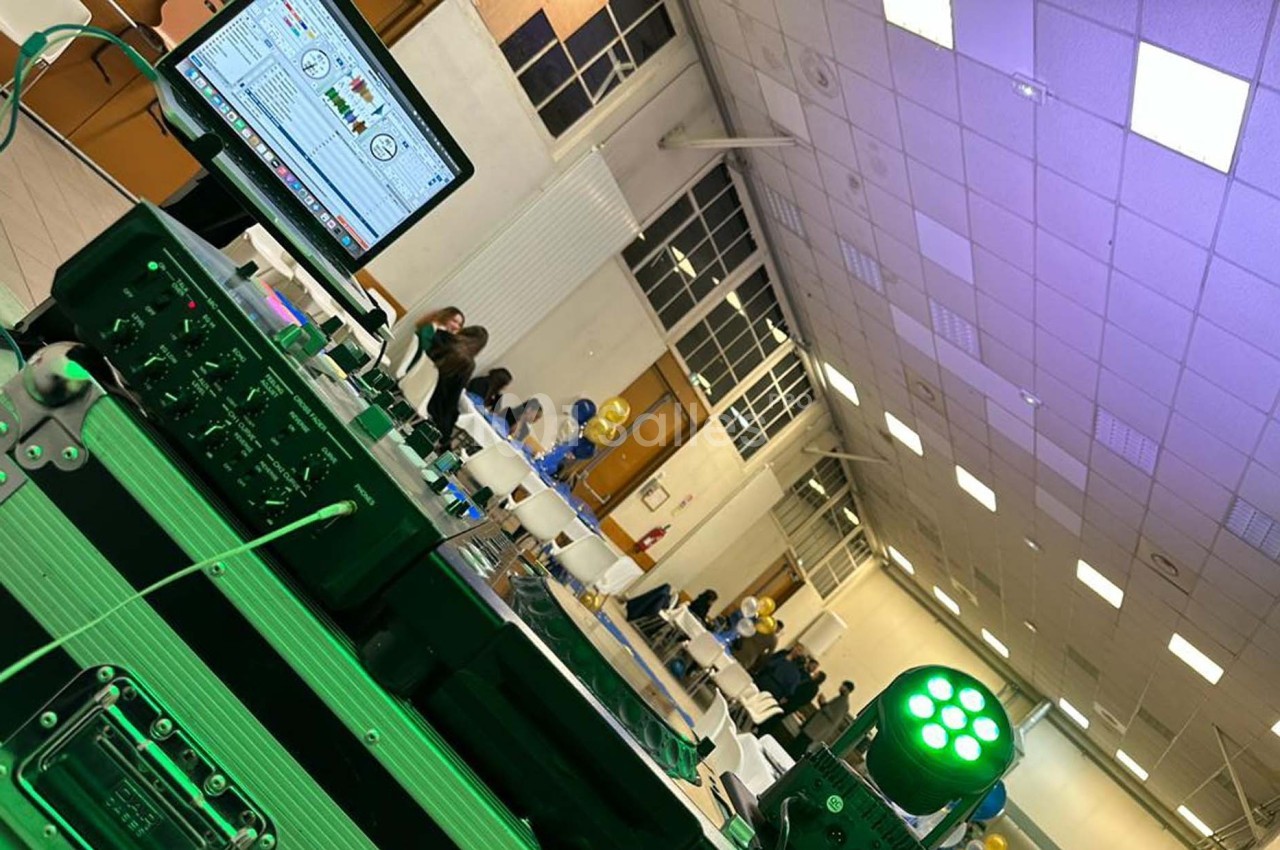 Vue d'une salle de réception avec des tables décorées, un équipement de sonorisation et des invités en arrière-plan.