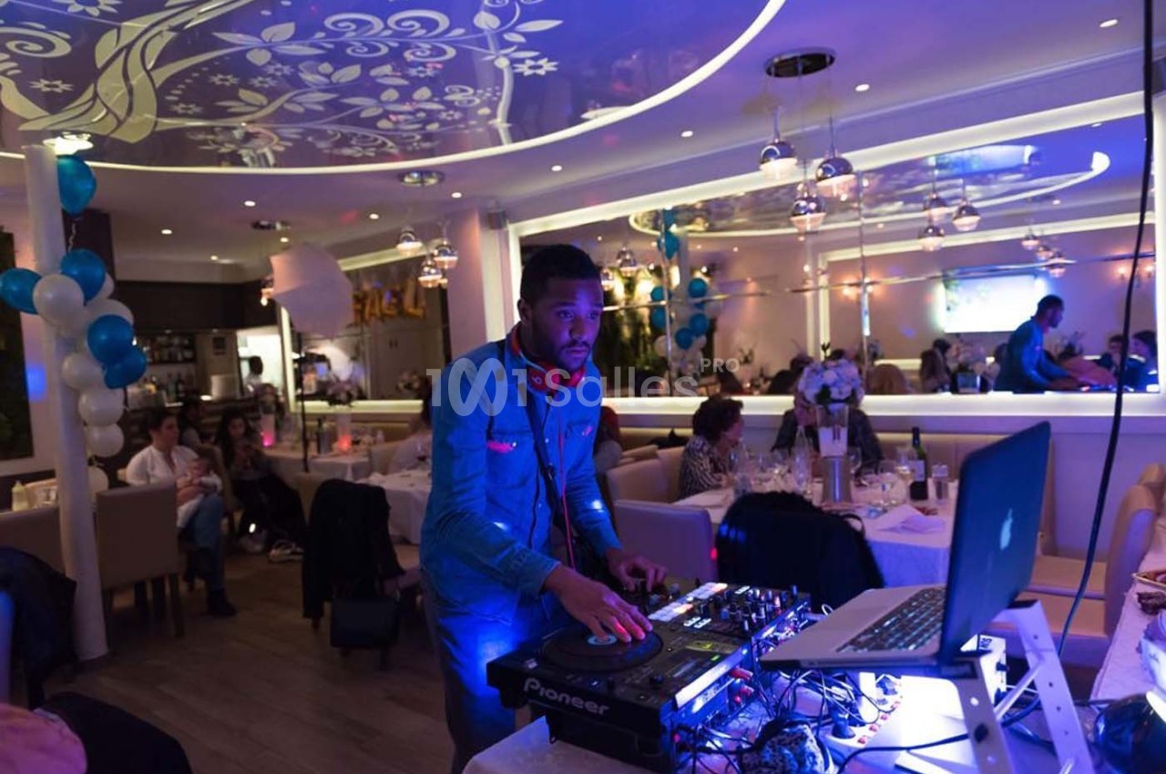 Un DJ mixe de la musique dans un restaurant décoré avec des ballons et des lumières colorées.