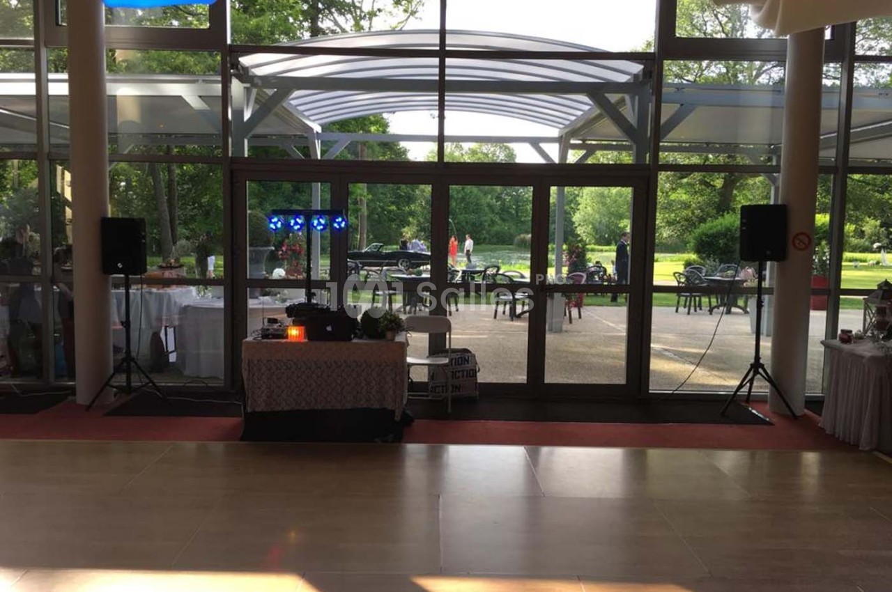 Salle lumineuse avec baie vitrée donnant sur un jardin, équipée d'une table de mixage et de haut-parleurs.