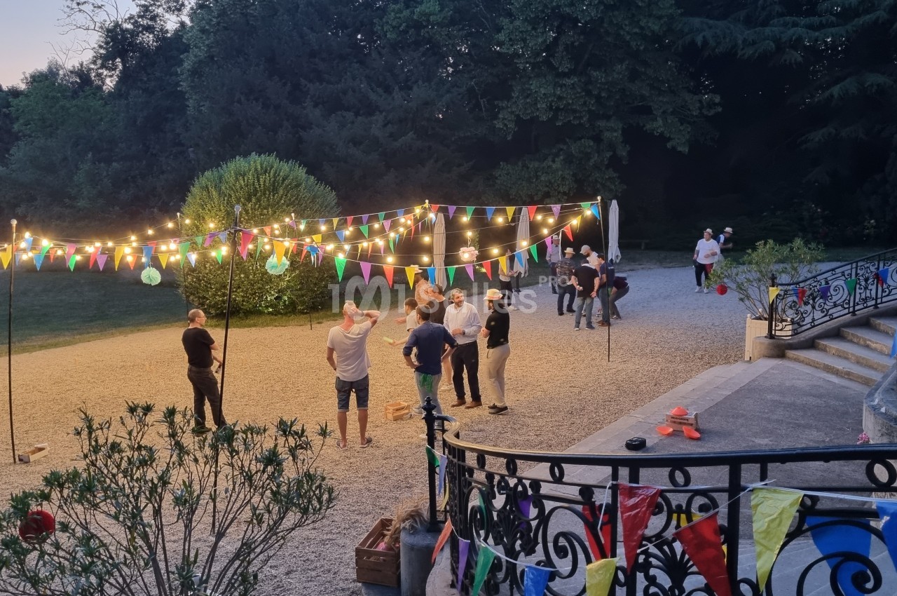 Personnes discutant dans une cour décorée de guirlandes lumineuses et de fanions colorés, en soirée en plein air.