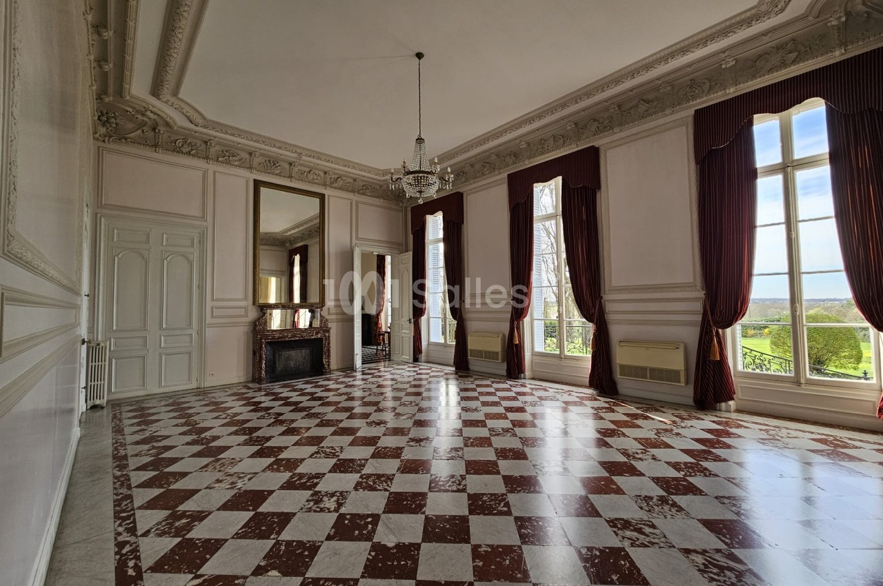 Salle spacieuse avec sol en damier rouge et blanc, grandes fenêtres, rideaux bordeaux et moulures décoratives au plafond.