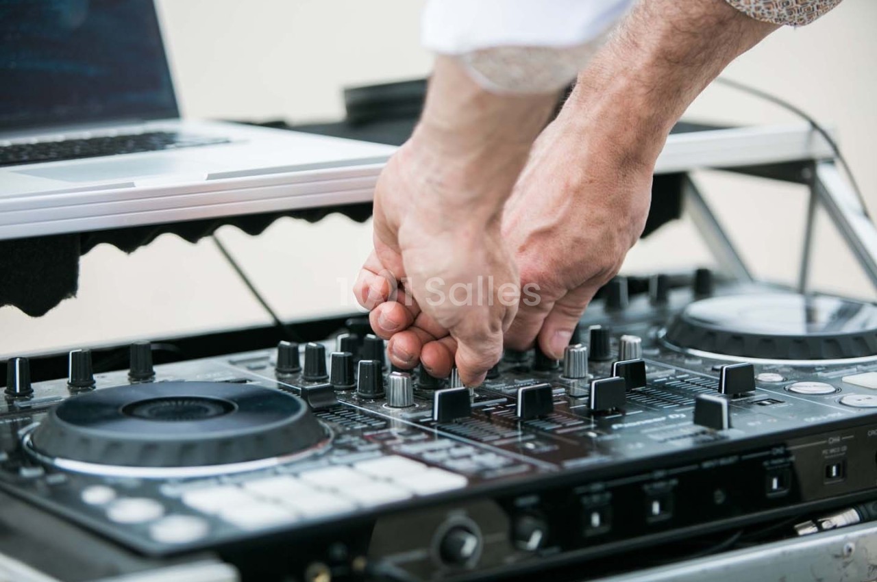 Mains ajustant les commandes d'une table de mixage DJ avec un ordinateur portable en arrière-plan.