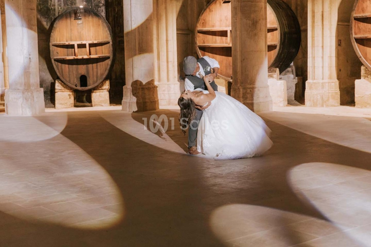Un couple danse dans une cave voûtée avec de grands tonneaux en bois en arrière-plan.