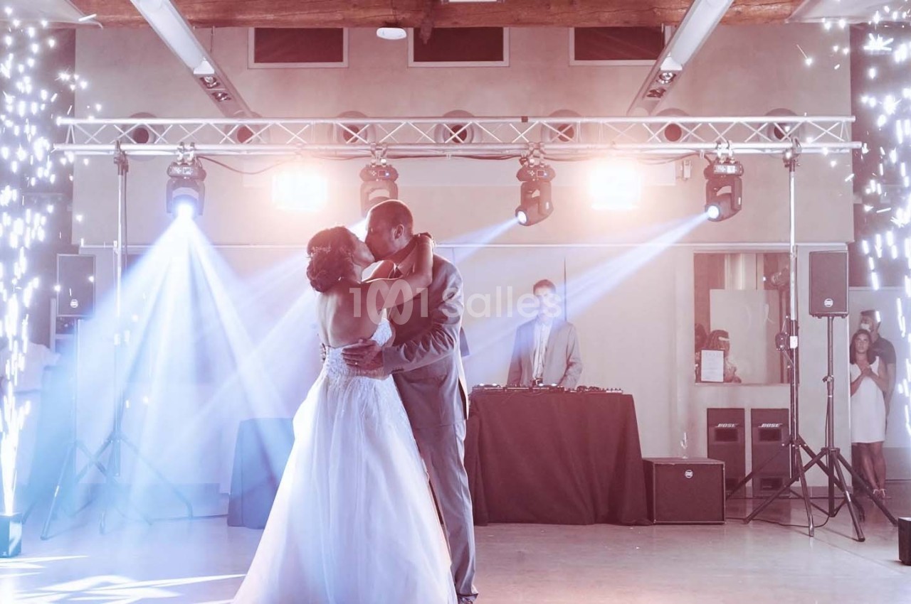 Un couple danse sous des jeux de lumière et des étincelles lors d'une réception avec un DJ en arrière-plan.