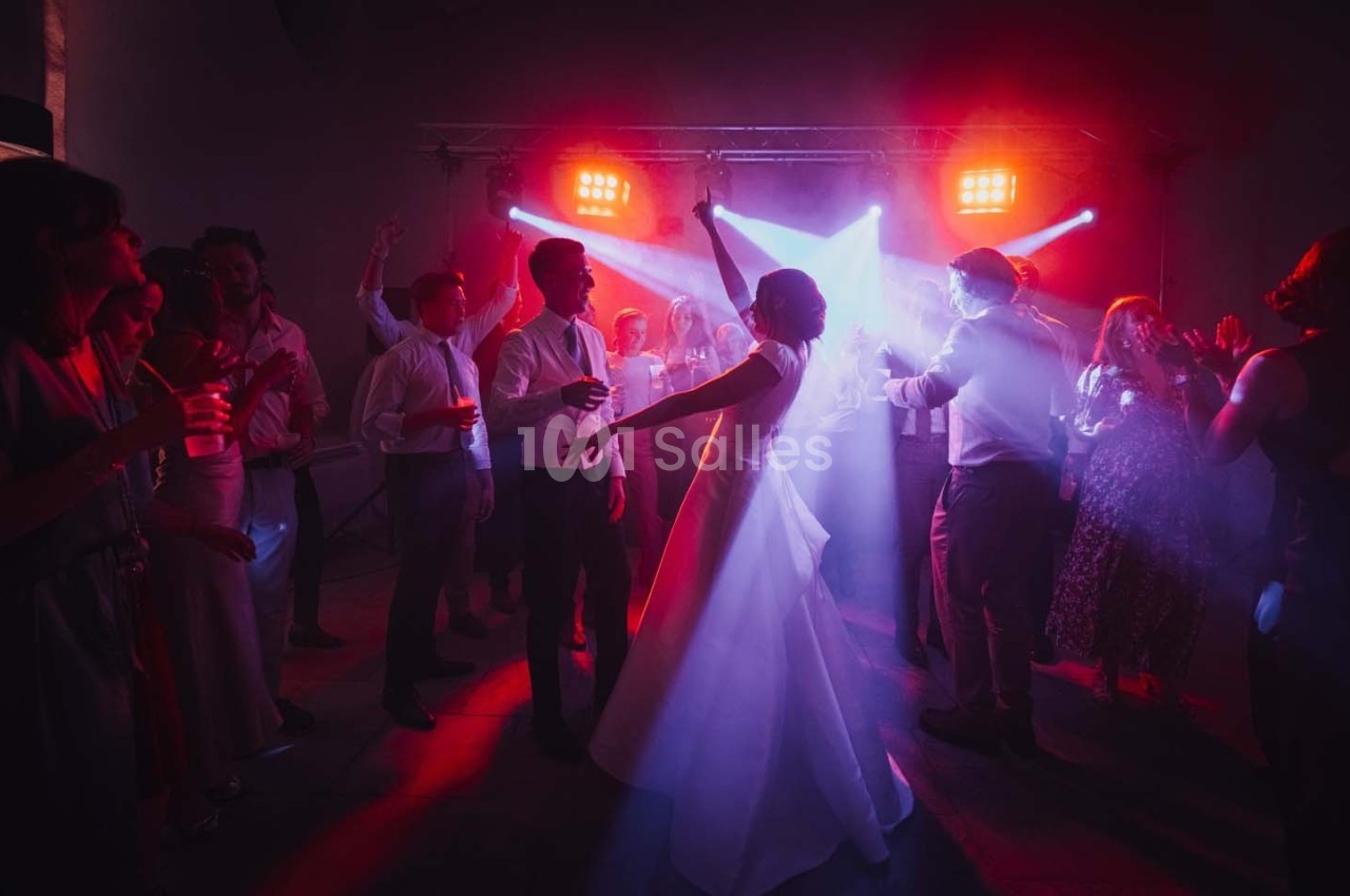 Un couple danse au centre d'une piste éclairée par des lumières colorées, entouré d'invités en fête.