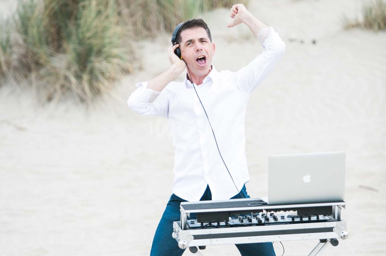 Un homme en chemise blanche utilise un équipement de DJ avec un ordinateur portable sur une plage.