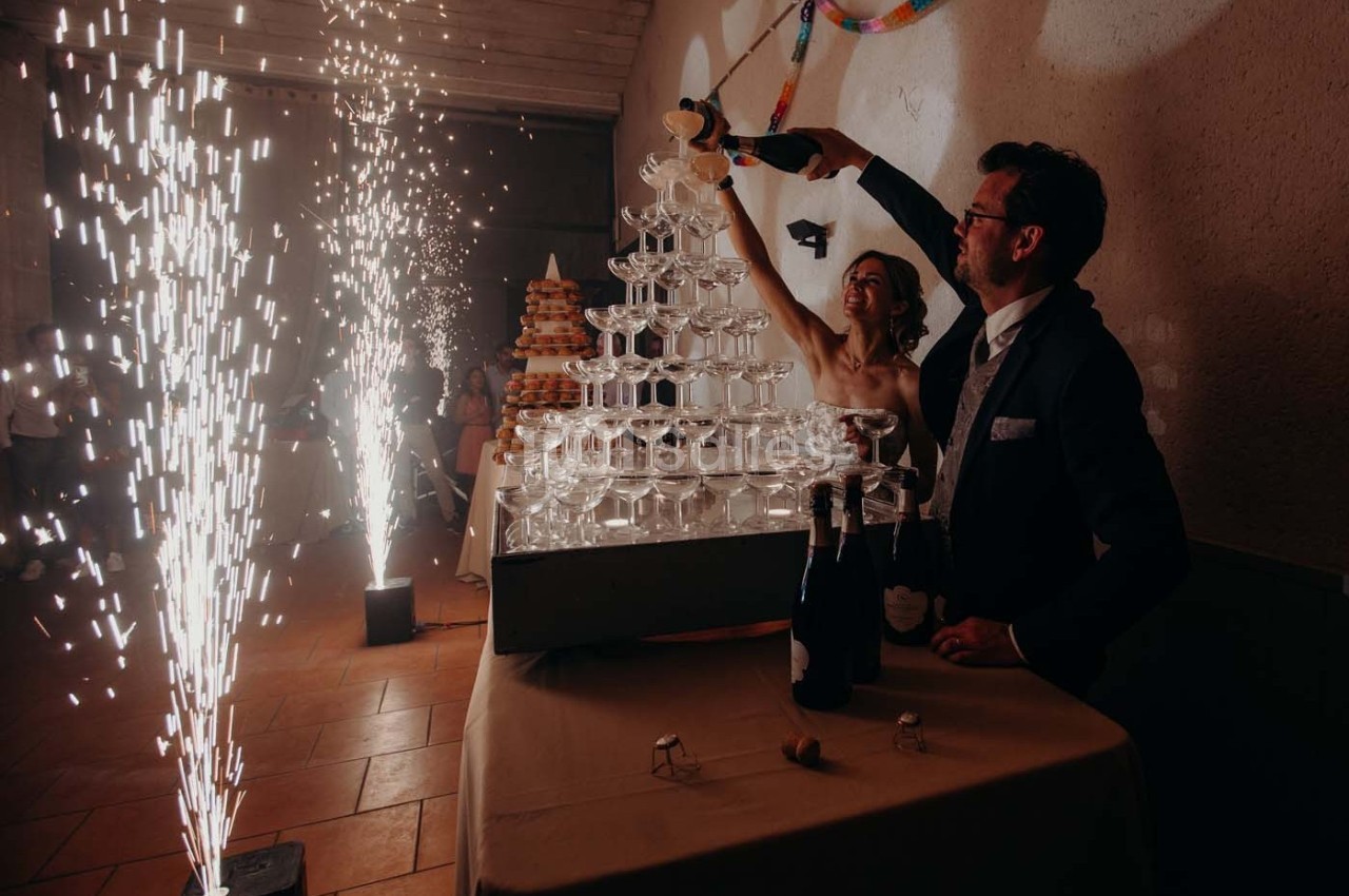Un couple remplit une pyramide de coupes de champagne lors d'une fête, entouré de jets d'étincelles.