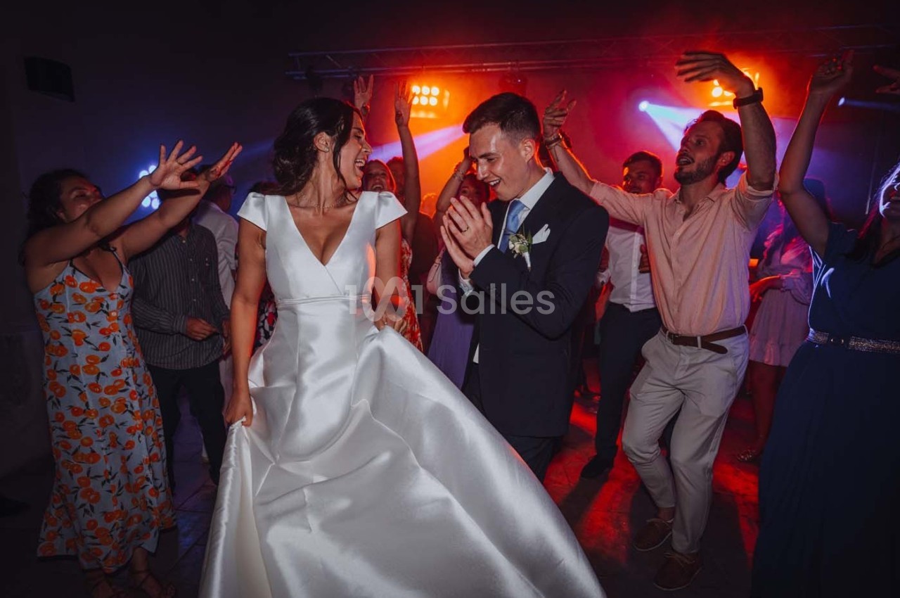 Un couple de mariés danse entouré d'invités sous des lumières colorées dans une ambiance festive.