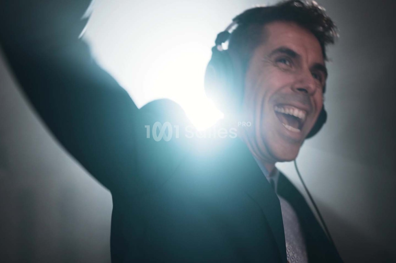 Homme souriant portant un casque audio, éclairé par une lumière vive en arrière-plan.