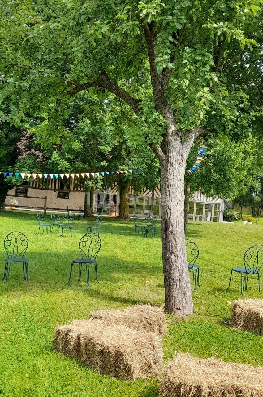 Chaises en métal et bottes de paille disposées sur une pelouse avec des arbres et des fanions colorés en arrière-plan.