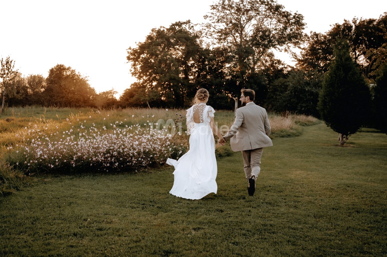 Un couple marche main dans la main dans un jardin au coucher du soleil, entouré de fleurs et d'arbres.