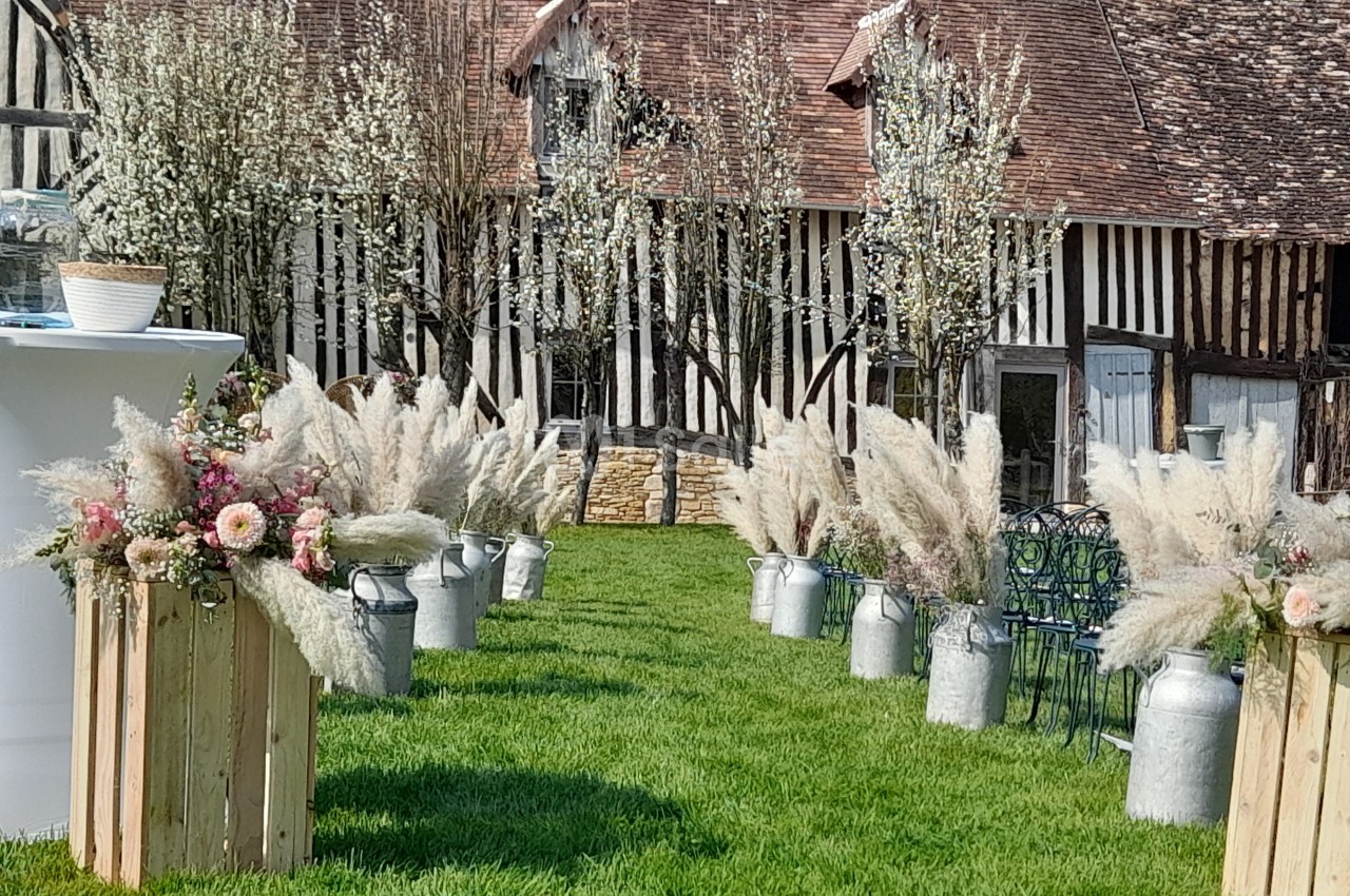 Allée décorée de fleurs séchées et d'herbes de la pampa, devant une maison à colombages et des arbres en fleurs.