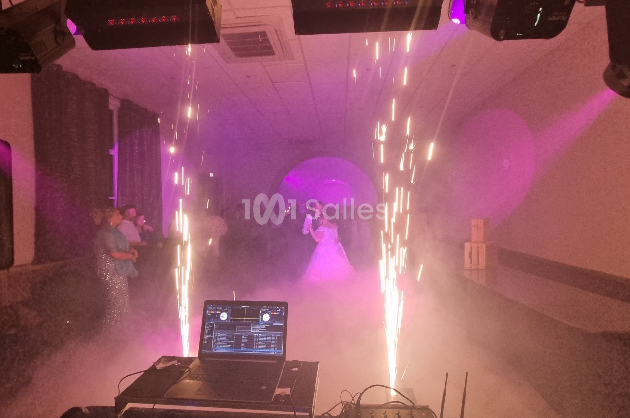 Un couple danse dans une salle éclairée par des lumières violettes, entouré de fumée et d'effets pyrotechniques.