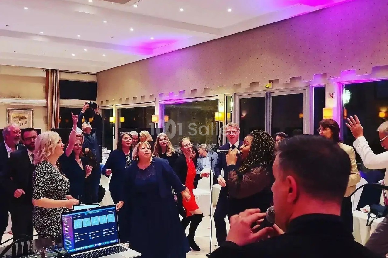 Des personnes dansent et chantent dans une salle éclairée de lumières colorées, avec un chanteur au premier plan.