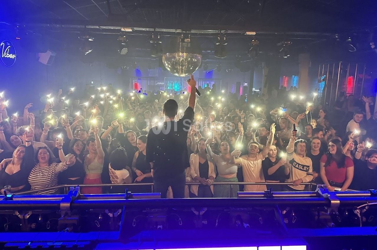 Un artiste sur scène face à une foule brandissant des téléphones allumés dans une salle de concert.