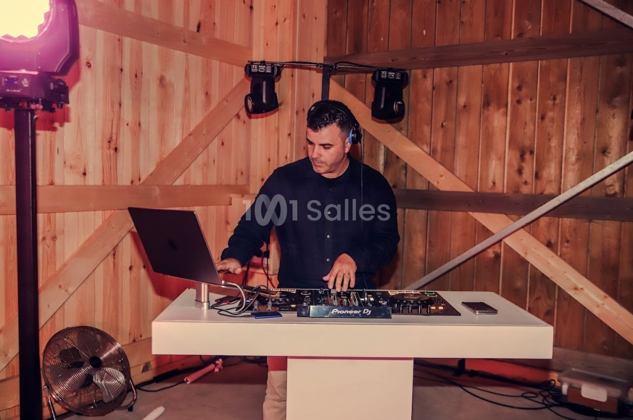 Un DJ mixe de la musique sur une table de mixage dans un espace en bois éclairé.