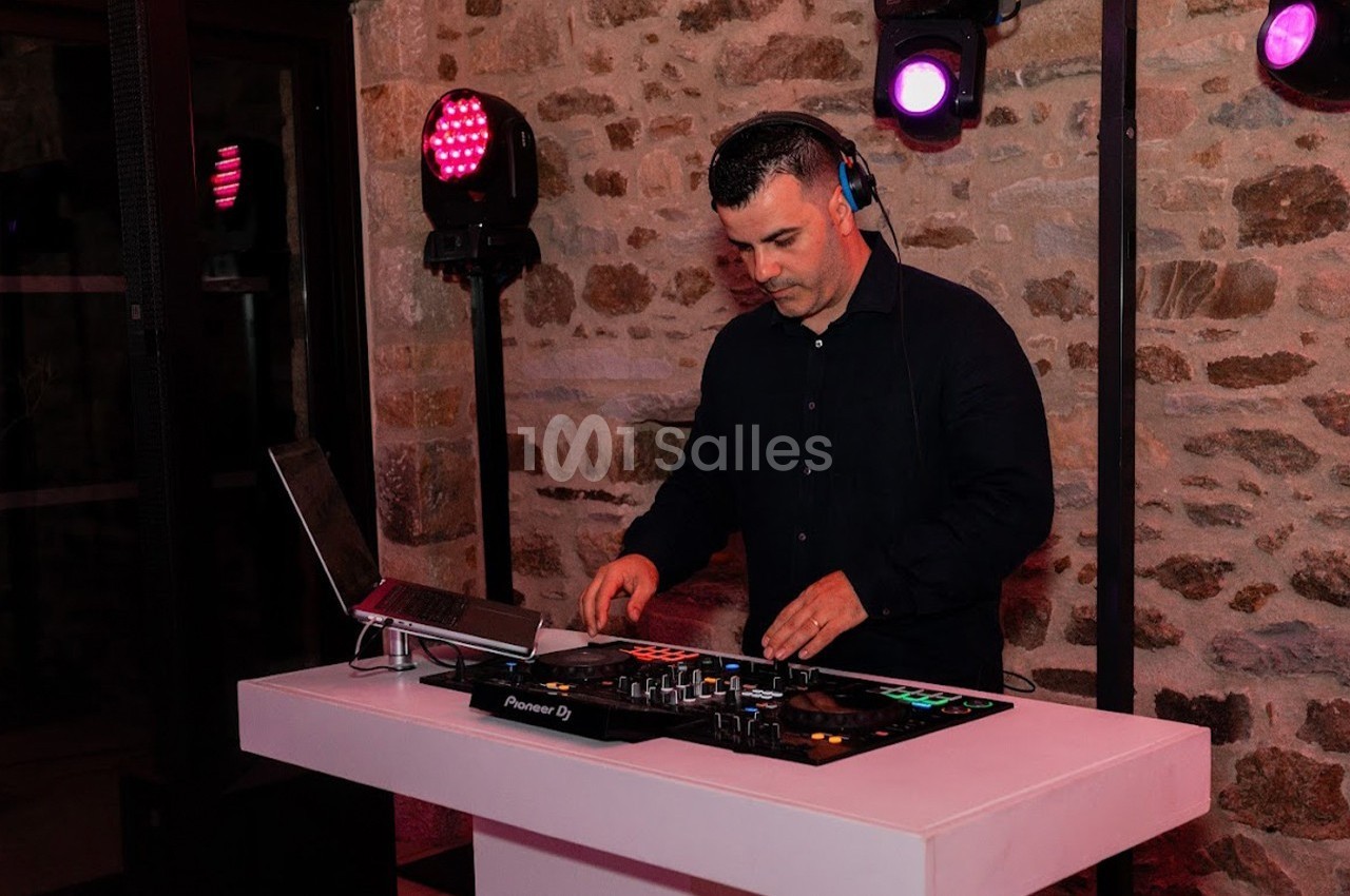 Un DJ mixant de la musique sur une table de mixage dans une salle en pierre éclairée par des lumières colorées.