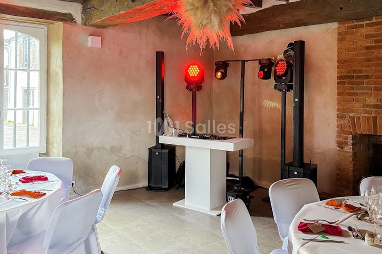 Table de mixage et éclairage rouge installés dans une salle de réception avec murs en pierre et tables dressées.