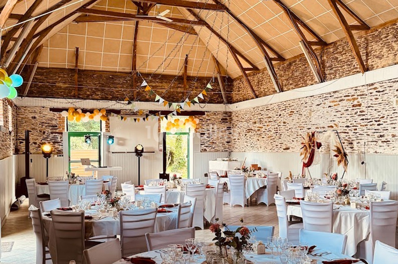 Salle de réception décorée pour un événement, avec tables dressées, guirlandes et ballons colorés.