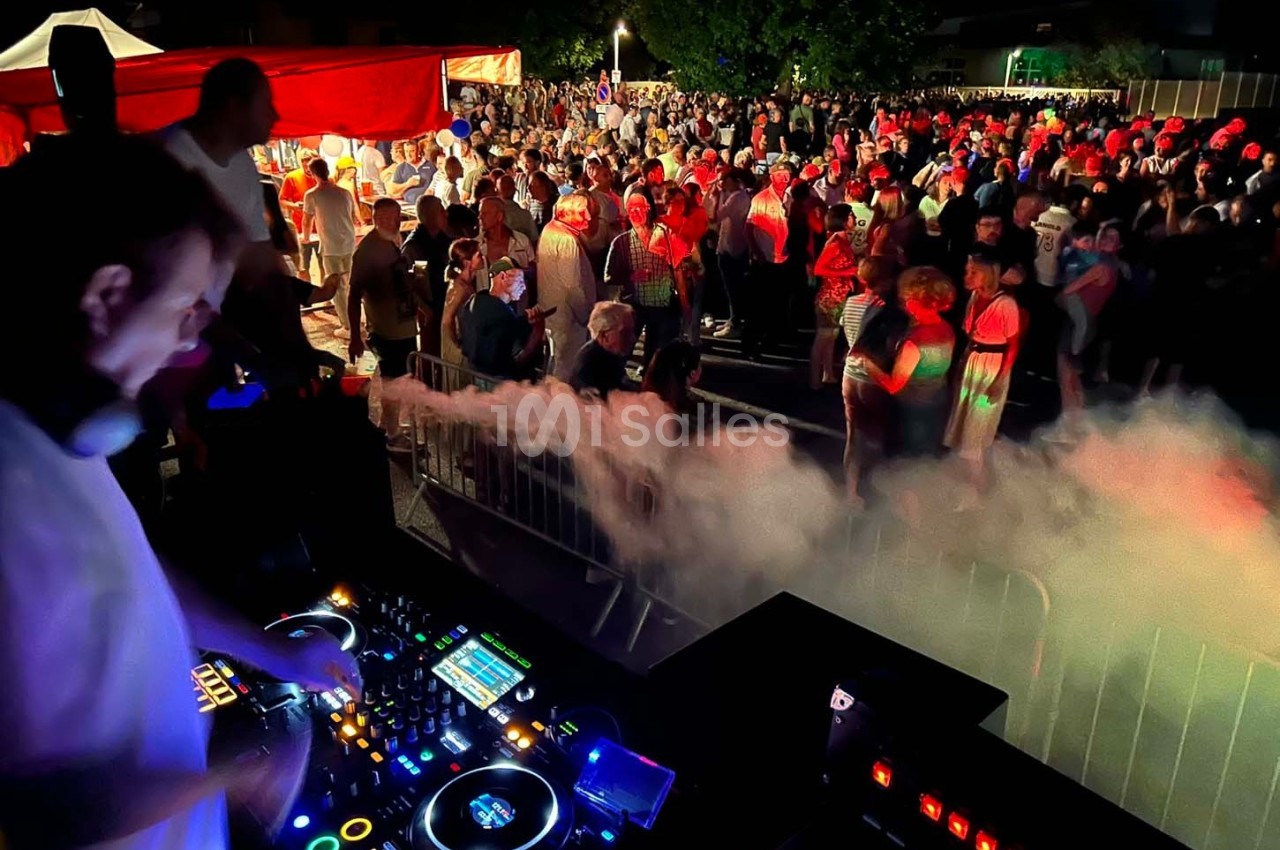 Un DJ mixe sur une scène en plein air devant une foule rassemblée de nuit, éclairée par des lumières colorées.