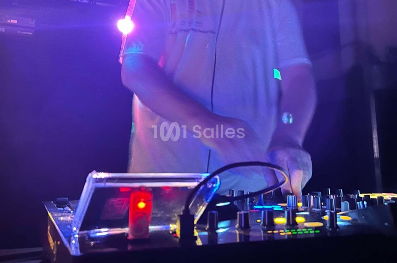 Un DJ mixant de la musique sur une table de mixage éclairée par des lumières colorées dans une ambiance sombre.
