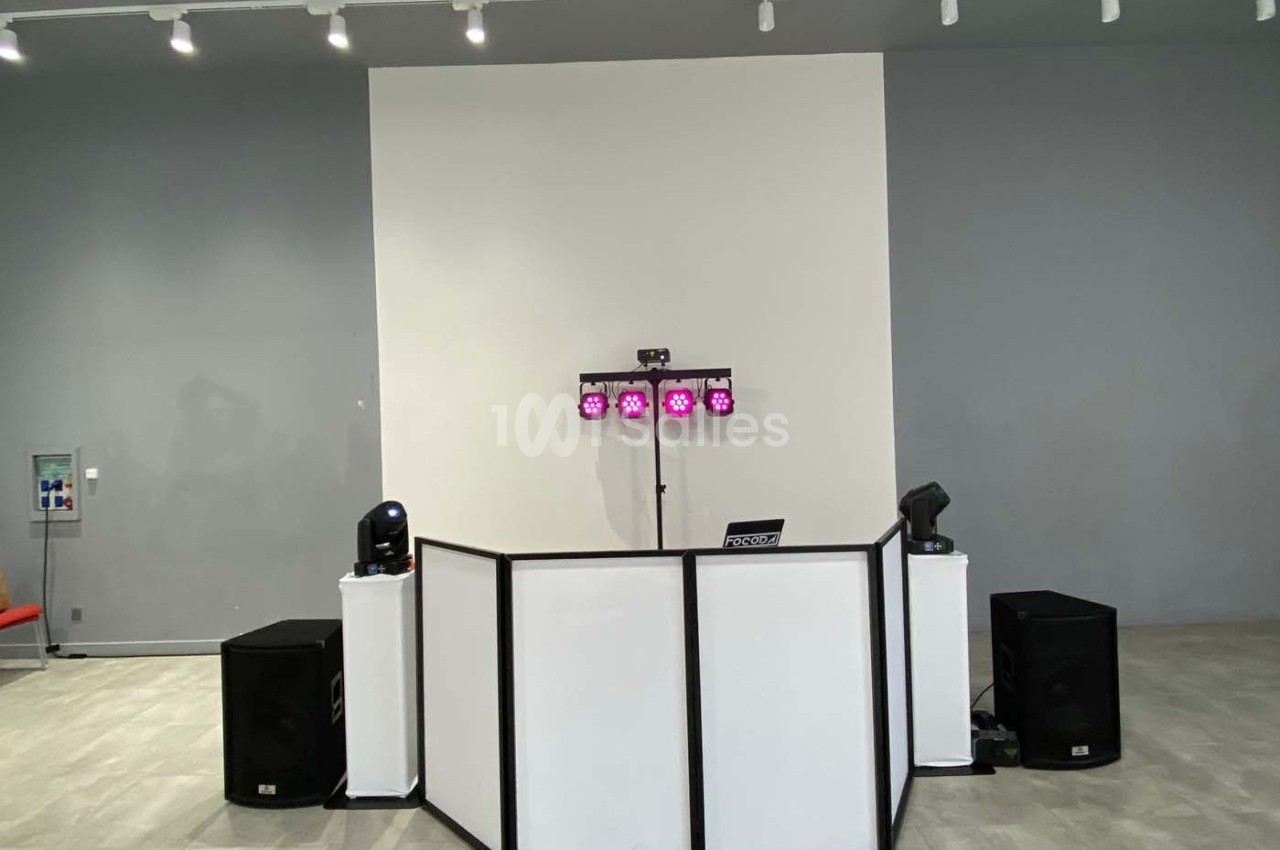 Poste de DJ avec une table blanche, des enceintes noires, des projecteurs colorés et un éclairage d'ambiance dans une salle…