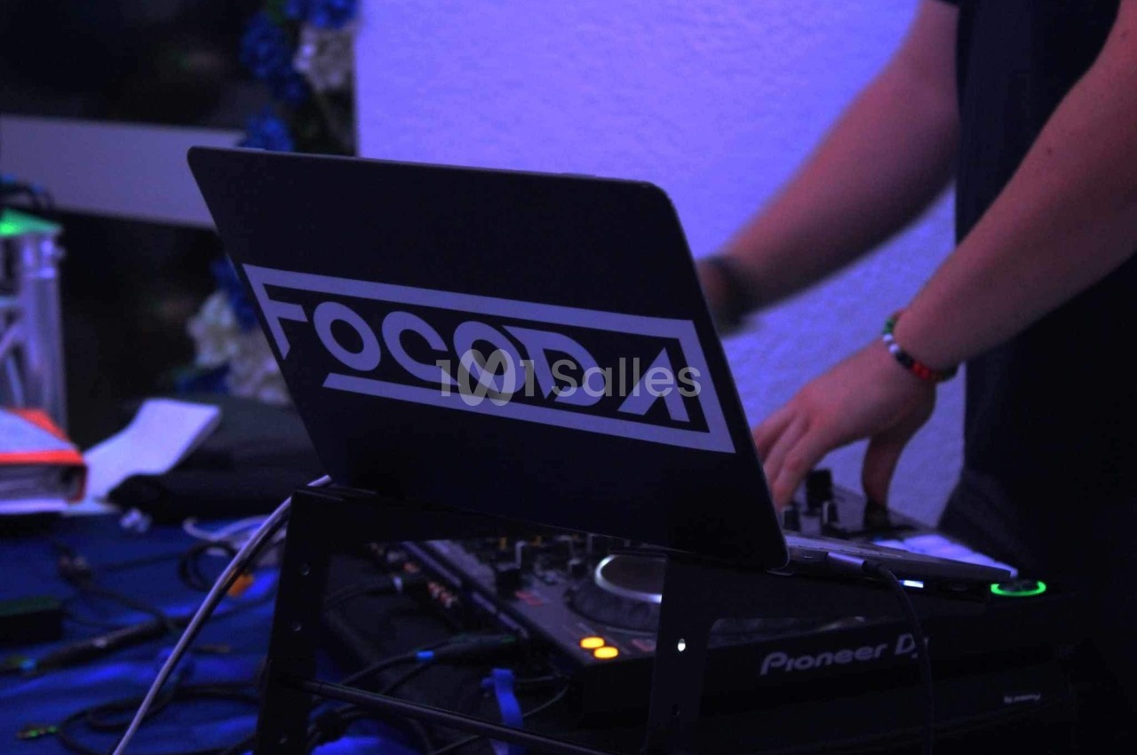 Un DJ mixant sur une table de mixage, avec un ordinateur portable affichant le logo ’FOCODA’.