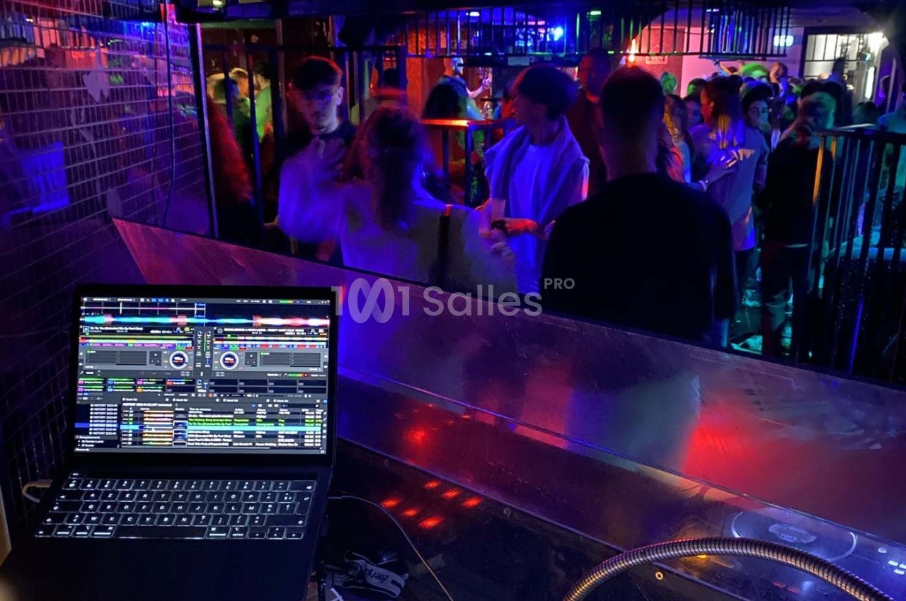 Vue d'une piste de danse animée depuis une cabine de DJ avec un ordinateur affichant un logiciel de mixage.