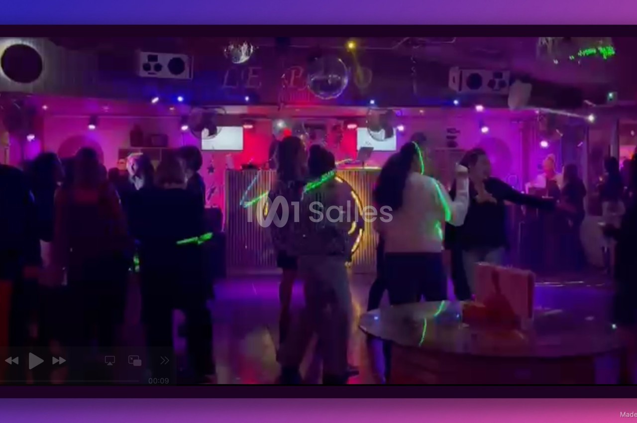 Des personnes dansent dans une salle de fête éclairée par des lumières colorées et des projecteurs.