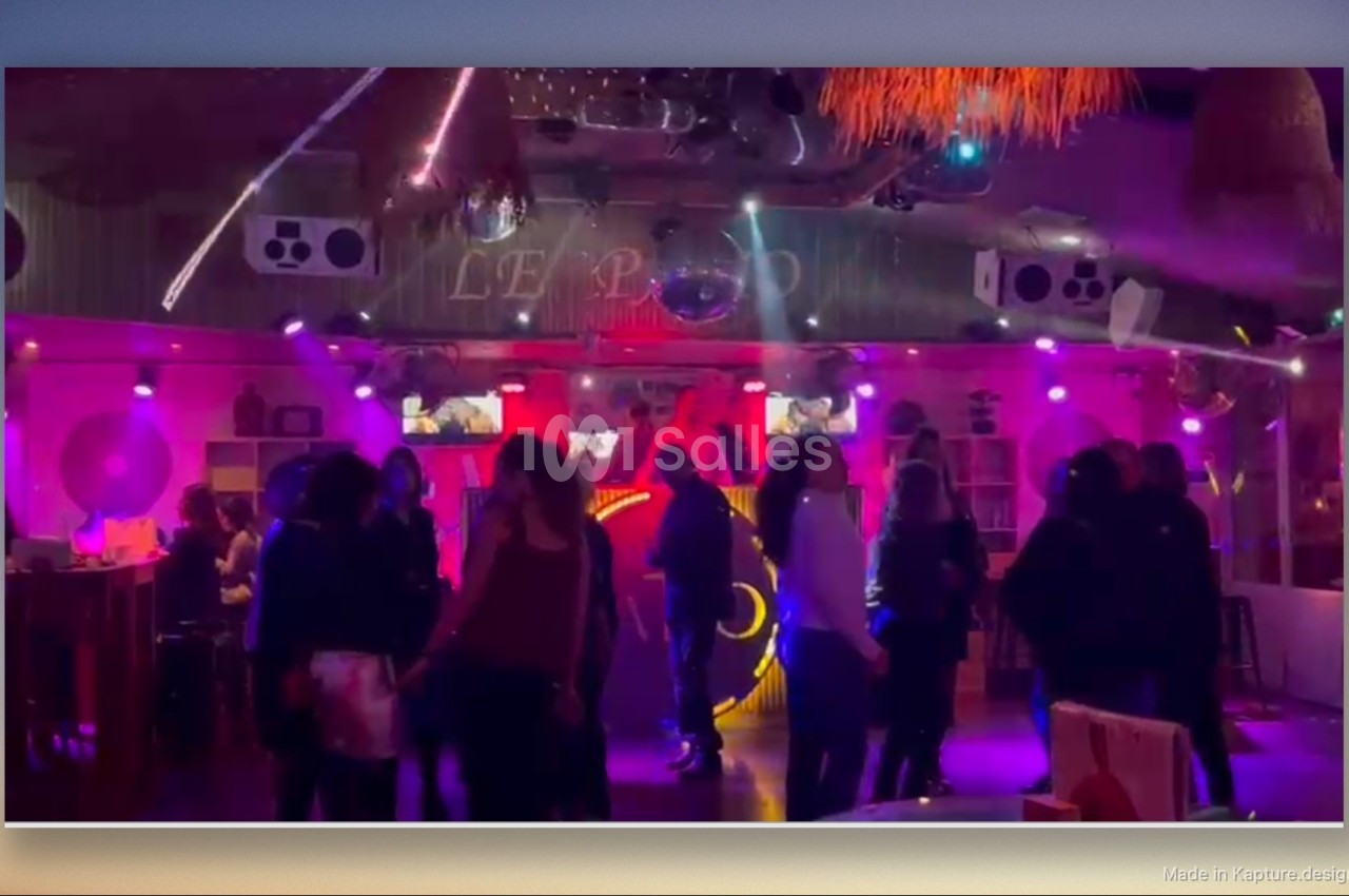 Des personnes dansent dans une salle éclairée par des lumières colorées, avec une ambiance festive et musicale.
