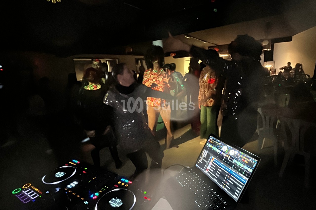 Personnes dansant dans une ambiance festive et sombre, avec une table de mixage et un ordinateur au premier plan.