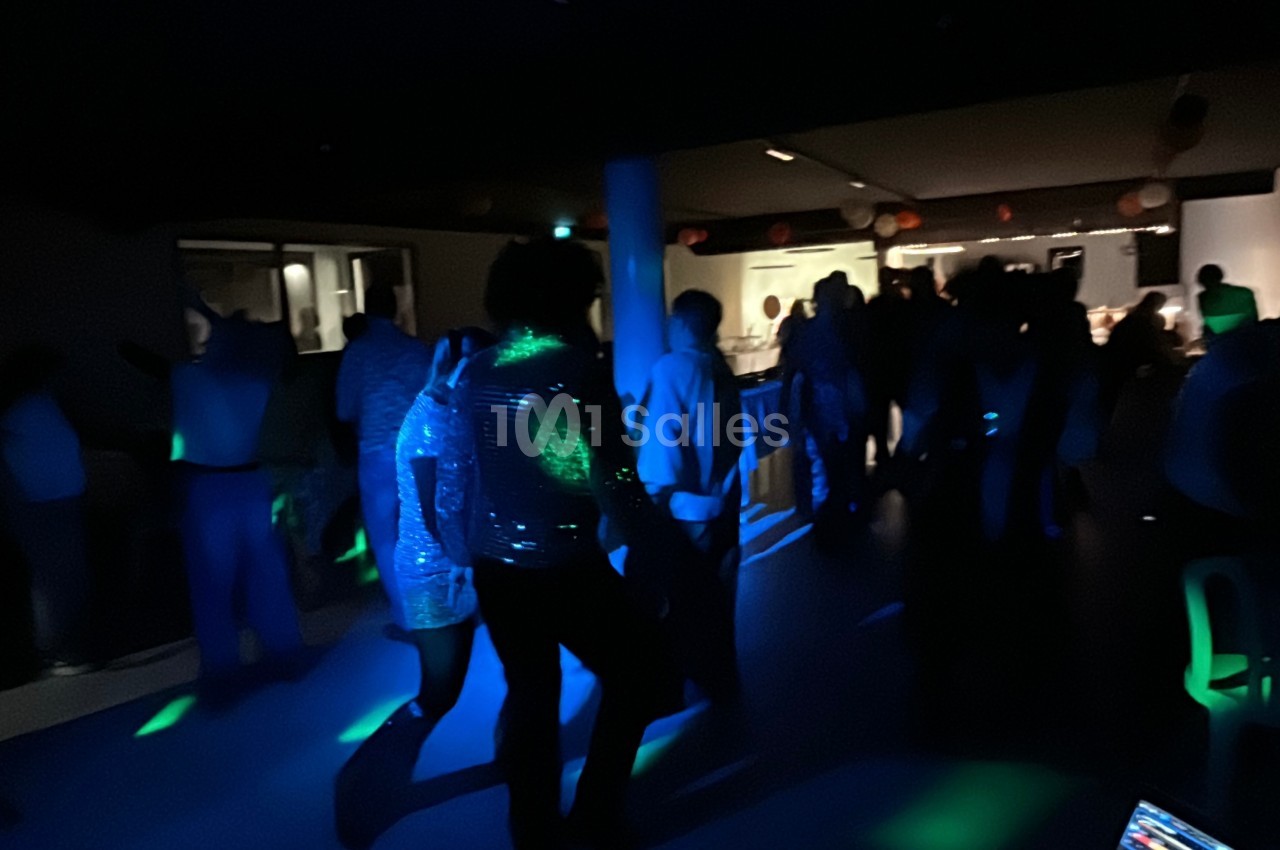 Des personnes dansent dans une salle faiblement éclairée avec des lumières colorées et une ambiance festive.