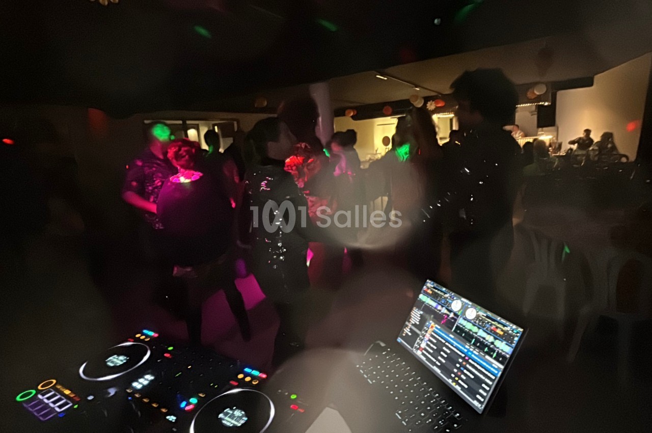 Personnes dansant dans une salle faiblement éclairée, avec une table de mixage et un ordinateur au premier plan.