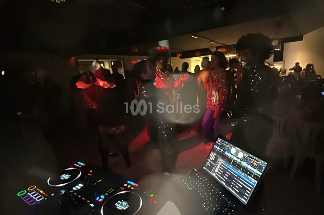 Personnes dansant dans une ambiance festive et tamisée, avec une table de mixage et un ordinateur au premier plan.