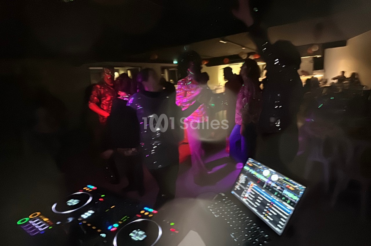 Personnes dansant dans une ambiance festive avec des lumières colorées, vue depuis une table de mixage de DJ.