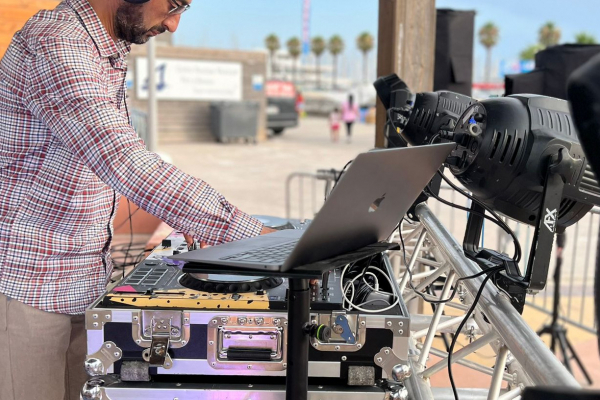 Un DJ mixe de la musique sur une table équipée d'un ordinateur portable et de matériel audio en extérieur.