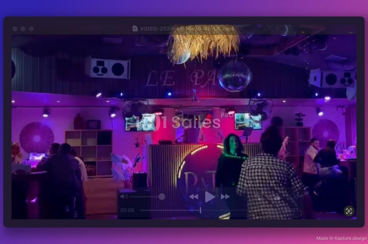 Personnes dansant et discutant dans un bar à l'ambiance tamisée avec éclairages colorés et une cabine de DJ.