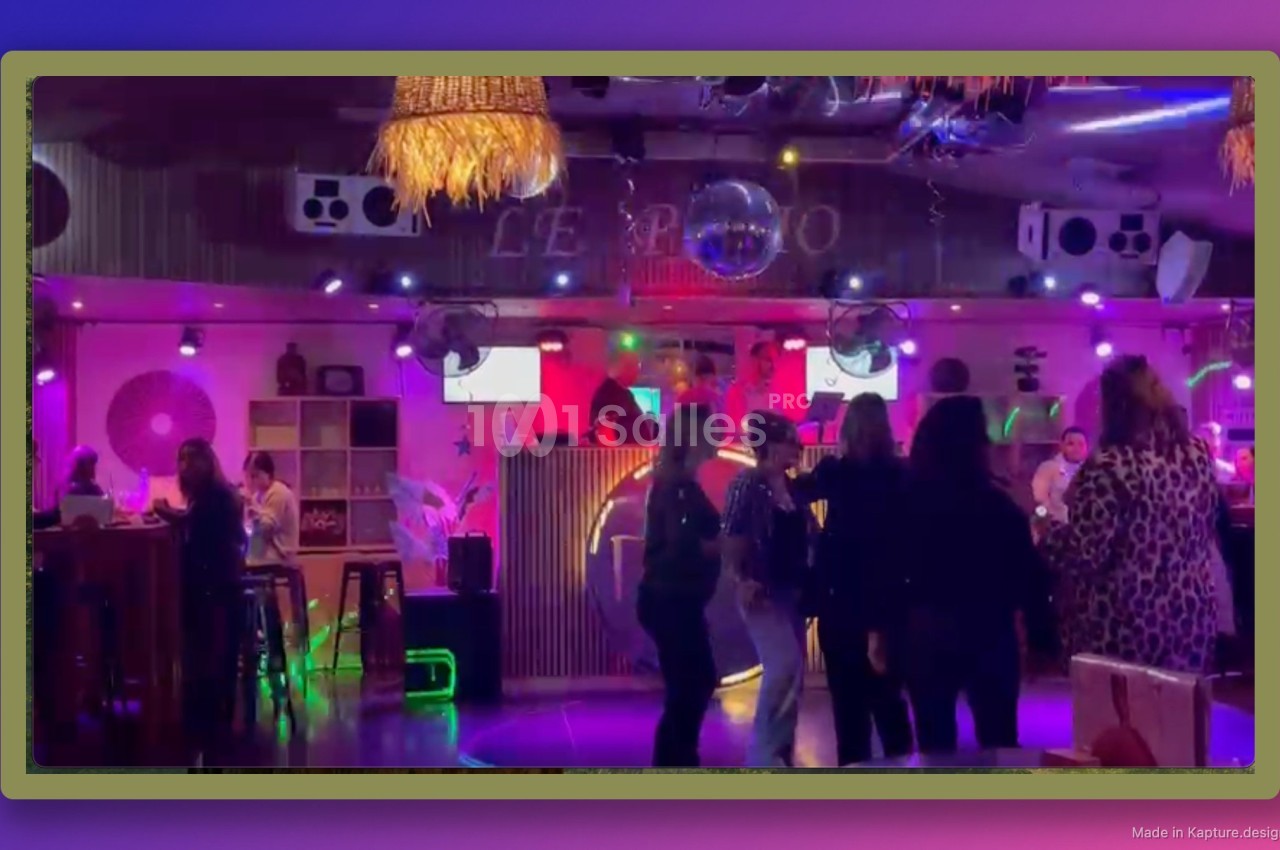 Personnes dansant et socialisant dans un bar ou club coloré avec une piste éclairée et un DJ en arrière-plan.