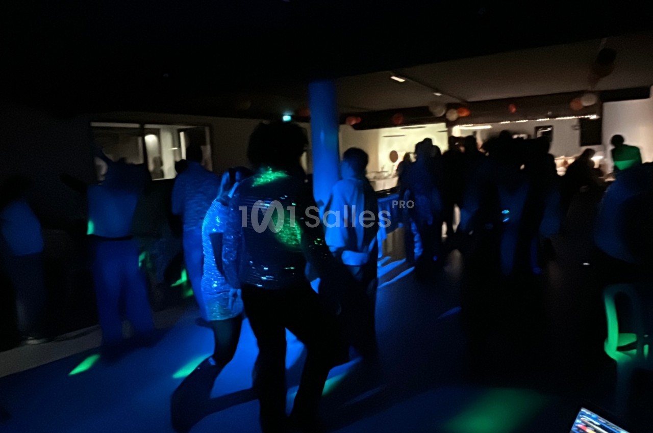 Des personnes dansent dans une salle faiblement éclairée avec des lumières colorées et une ambiance festive.