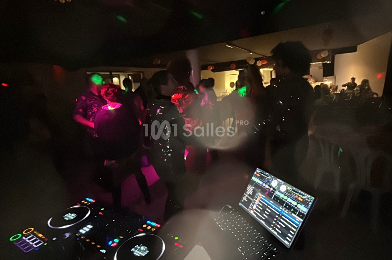 Personnes dansant dans une salle faiblement éclairée, avec une table de mixage et un ordinateur au premier plan.