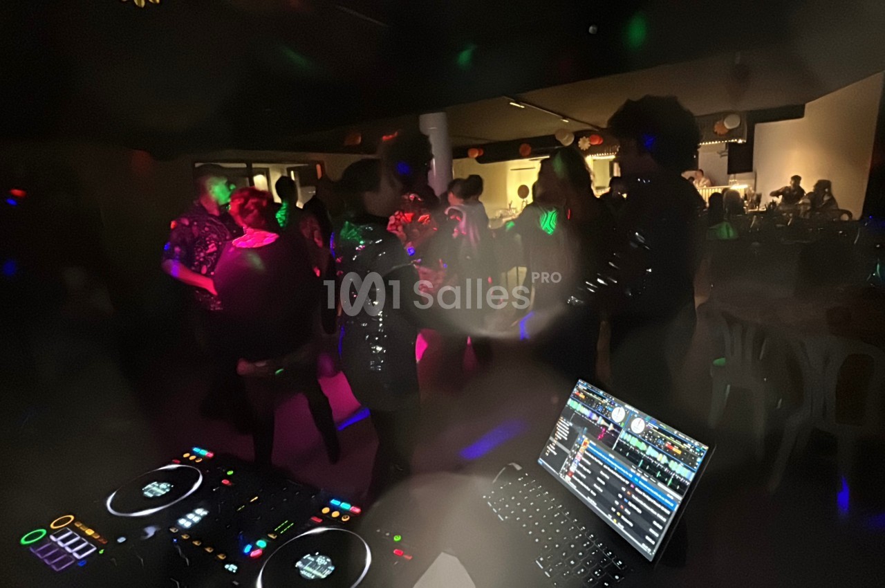 Personnes dansant dans une salle sombre éclairée par des lumières colorées, avec une table de DJ au premier plan.