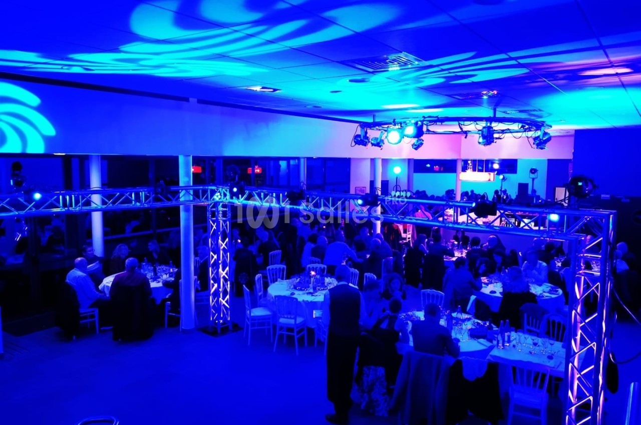 Salle de réception illuminée de lumières bleues, avec des invités assis à des tables rondes.