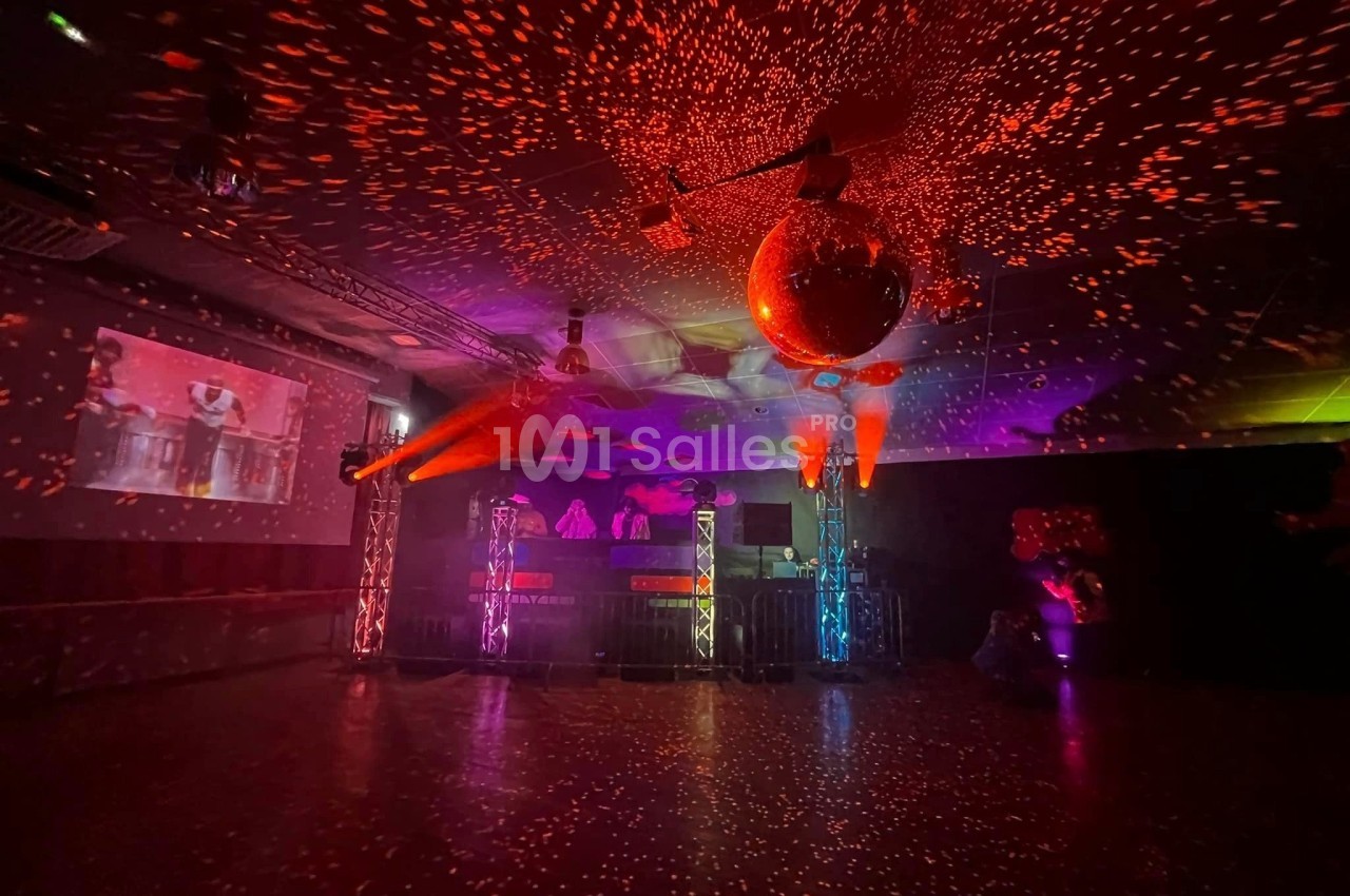 Salle de fête sombre avec éclairages colorés, projecteurs, boule à facettes et écran projetant une image.