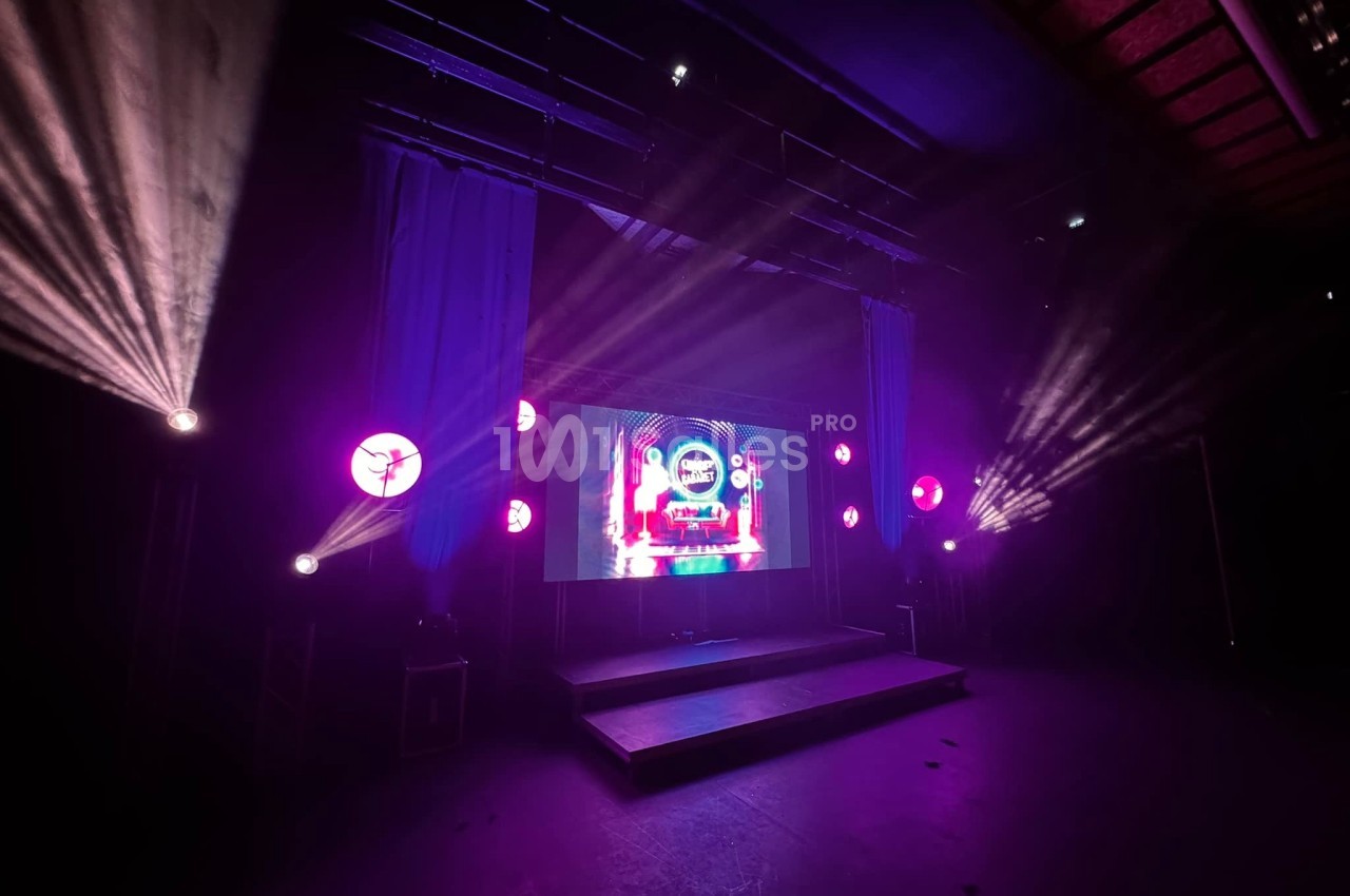 Scène éclairée avec projecteurs colorés et écran central affichant des graphismes lumineux dans une ambiance sombre.