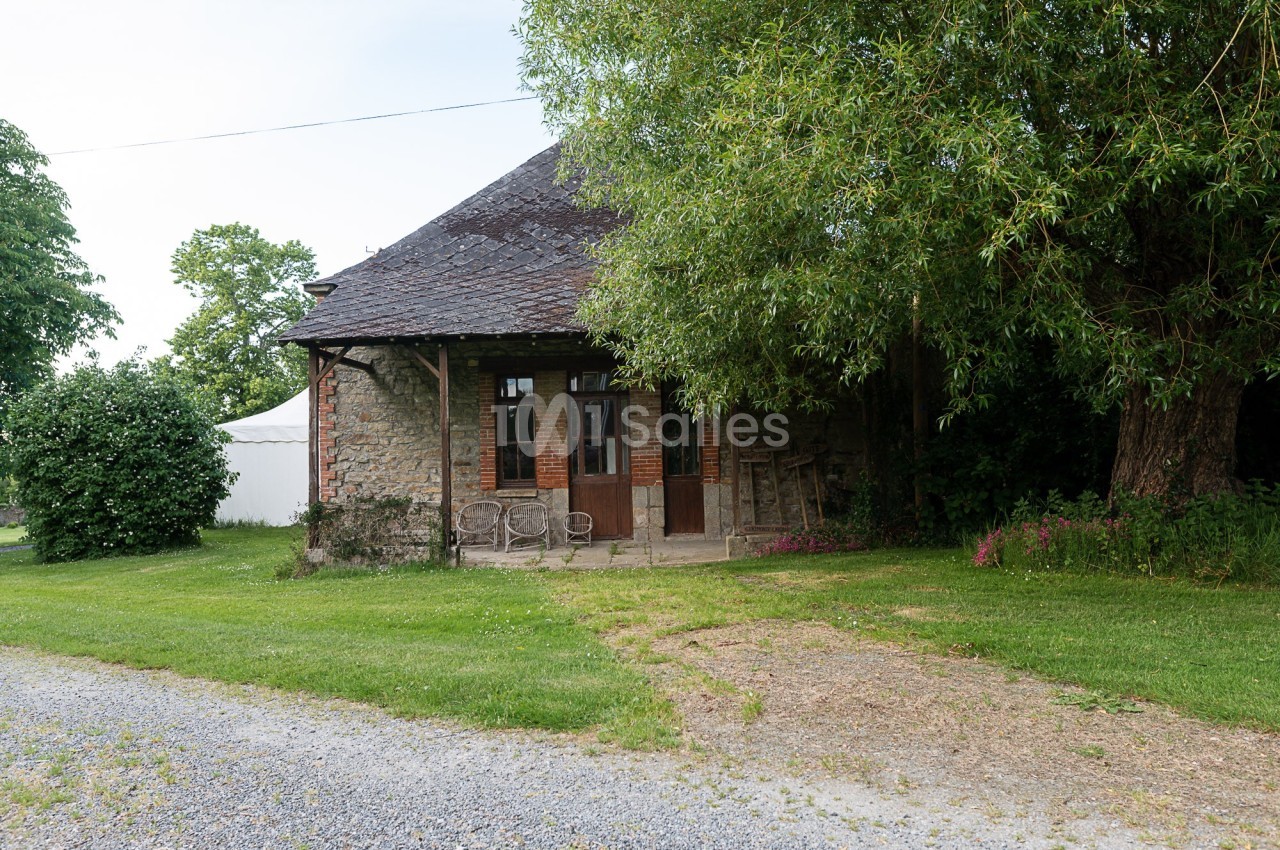 Maison en pierre avec toit en ardoise, entourée de verdure, avec une terrasse et des chaises en façade.