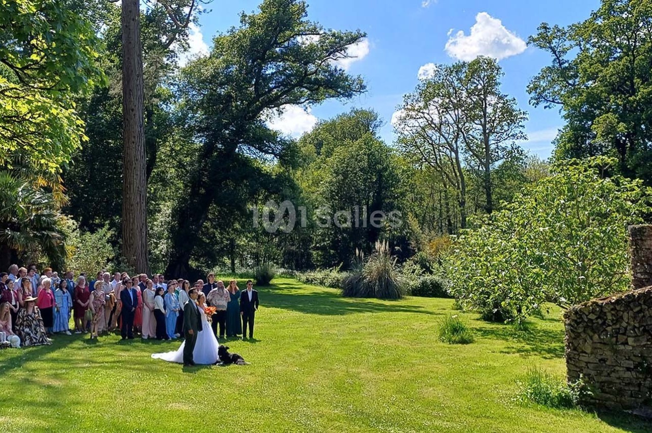 Un couple de mariés pose devant un groupe d'invités dans un jardin verdoyant par une journée ensoleillée.